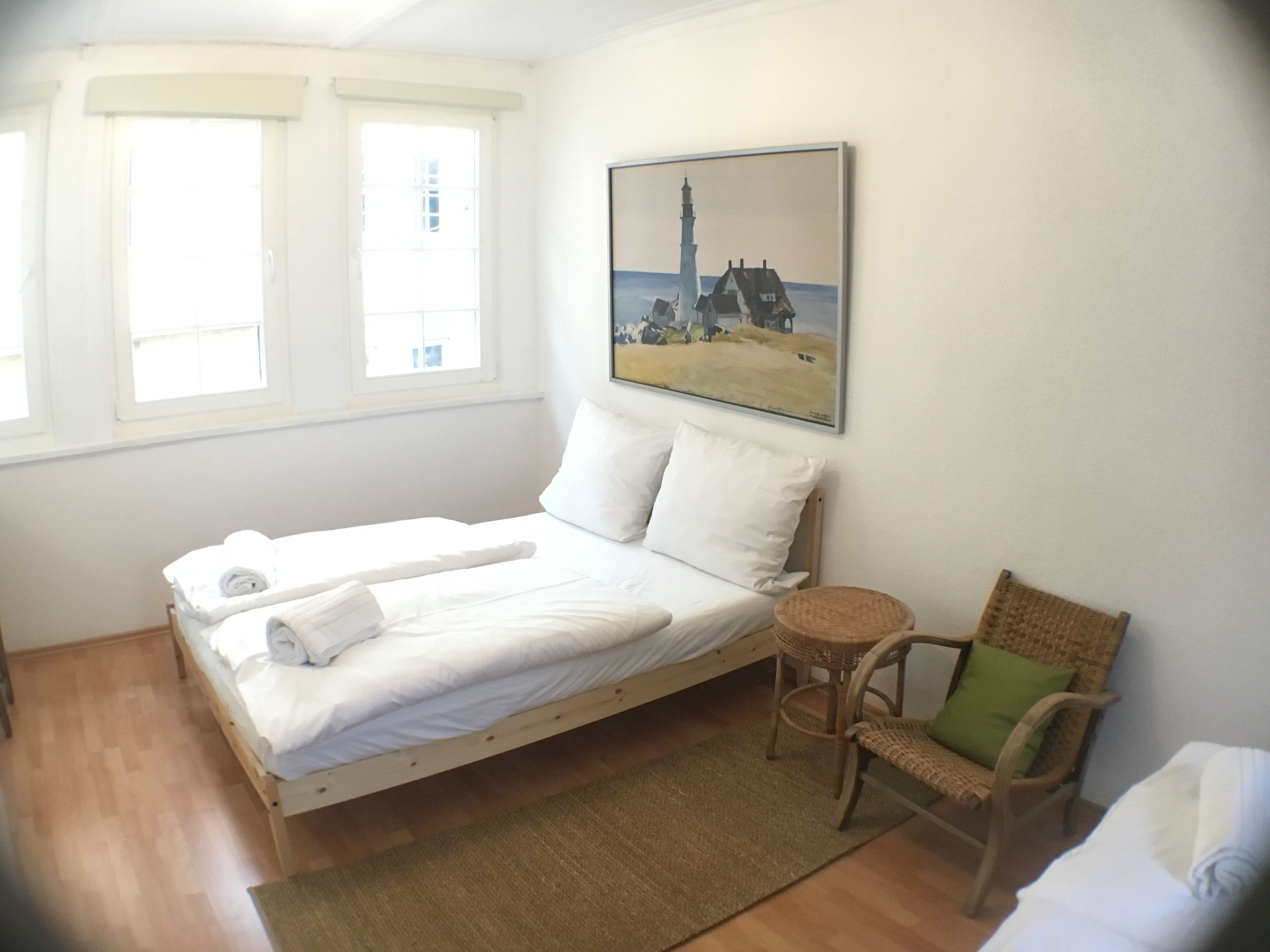 A bedroom with a bed, a chair, a rug, and a painting on the wall.
