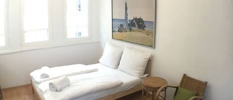A bedroom with a bed, a chair, a rug, and a painting on the wall.