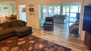 A spacious living area with a large sectional sofa, a smaller sofa, and a patterned rug. There is a dining area with a table and chairs visible through an open doorway.