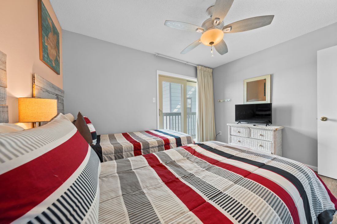 A hotel room with two beds, a ceiling fan, a TV, and a window with curtains.