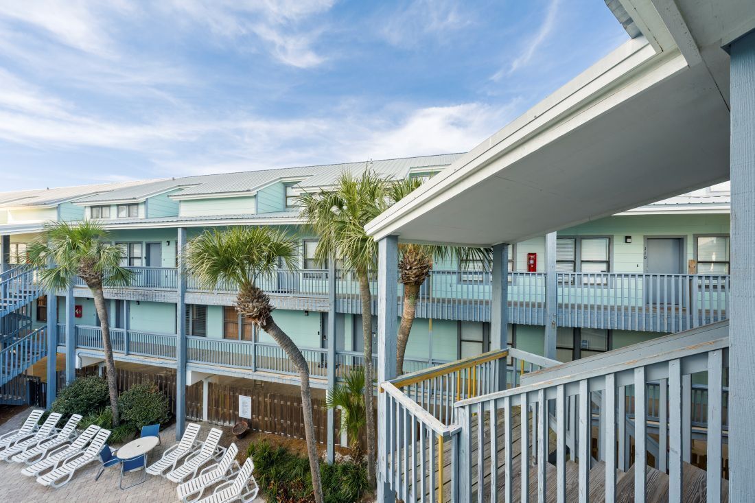 A multi-story hotel with balconies, palm trees, and outdoor seating.