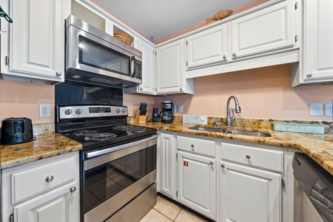A kitchen with white cabinets, a stainless steel stove, a microwave, a sink, and a coffee maker.
