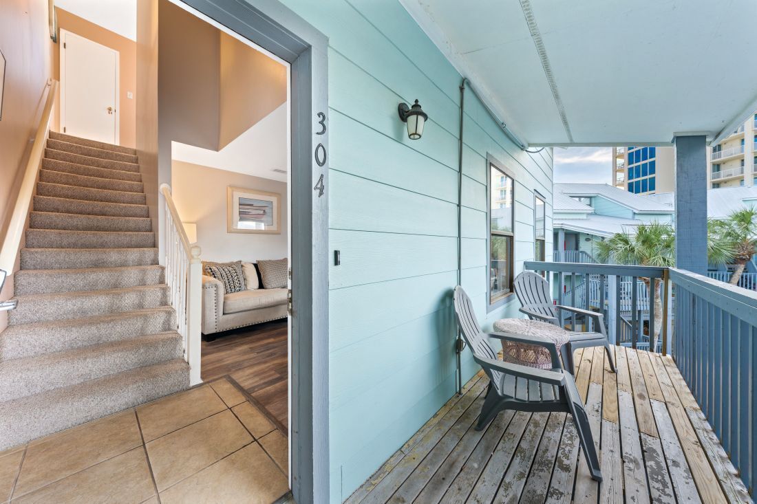 Une terrasse en bois avec des chaises, un escalier et un mur ext érieur bleu clair portant le numéro 304.