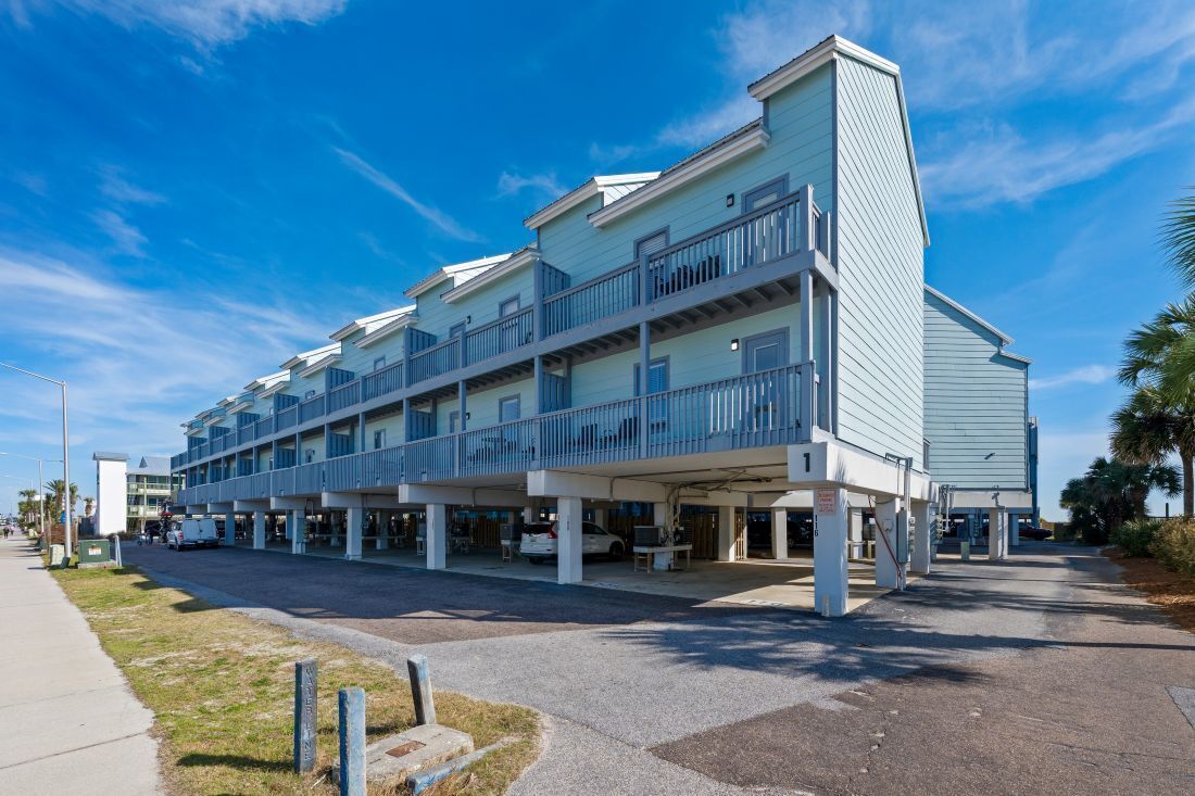 Un hotel a più piani con balconi, un'area di parcheggio coperta e un cielo sereno.