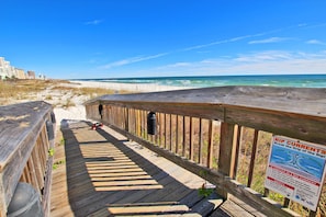 A wooden boardwalk leading to a beach with a sign warning about rip currents.