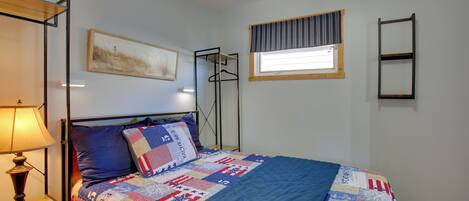 Ett sovrum med en säng, ett sängbord, en lampa, ett fönster med gardin, en vägghylla och en inramad tavla.