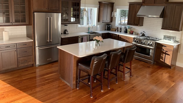 Een moderne keuken met houten kasten, roestvrijstalen apparatuur en een centraal eiland met barkrukken.