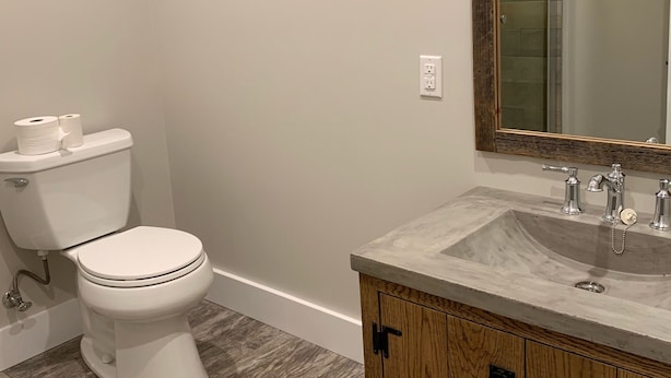 Une salle de bain avec des toilettes blanches, un meuble-lavabo en bois et un miroir au-dessus du meuble-lavabo.