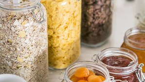 Diversos alimentos em potes de vidro com canudos, incluindo aveia, cereais e frutas secas.