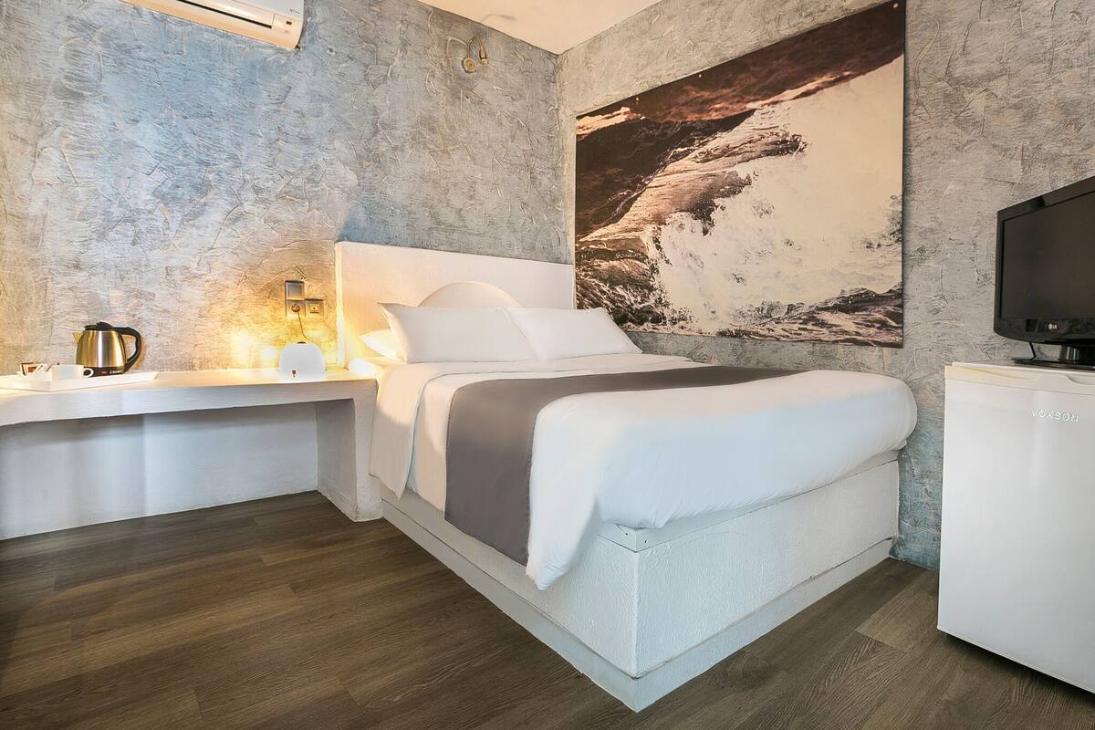 A modern bedroom with a large bed, a bedside table with a lamp, a TV, and a large wall mural.