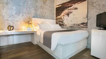 Quarto moderno com uma cama grande, mesa de cabeceira com abajur, televisão e um grande mural na parede.