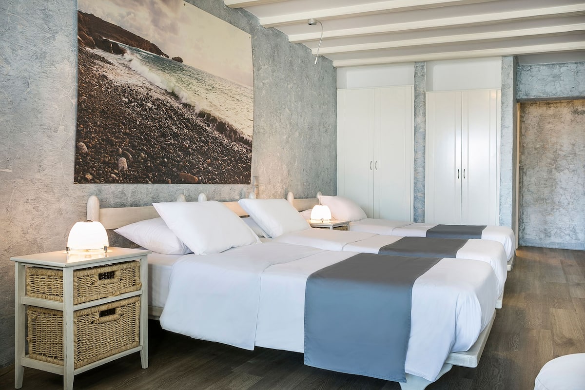 A bedroom with a large bed, a nightstand with baskets, a wall-mounted painting, and a wardrobe.