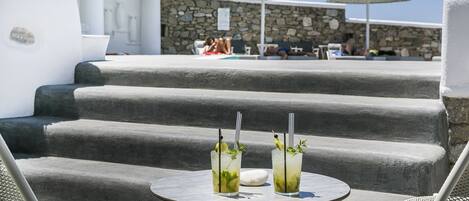 A terrace with two tables, each with a drink and a straw, and a stone wall in the background.