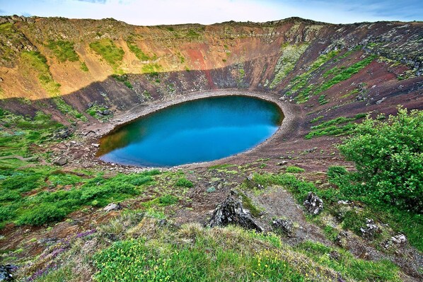 A crater lake surrounded by rugged terrain with sparse vegetation.