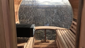 Une structure circulaire en bois, dotée d’un barbecue et d’un espace pour s’asseoir, qui offre une vue sur un paysage boisé.