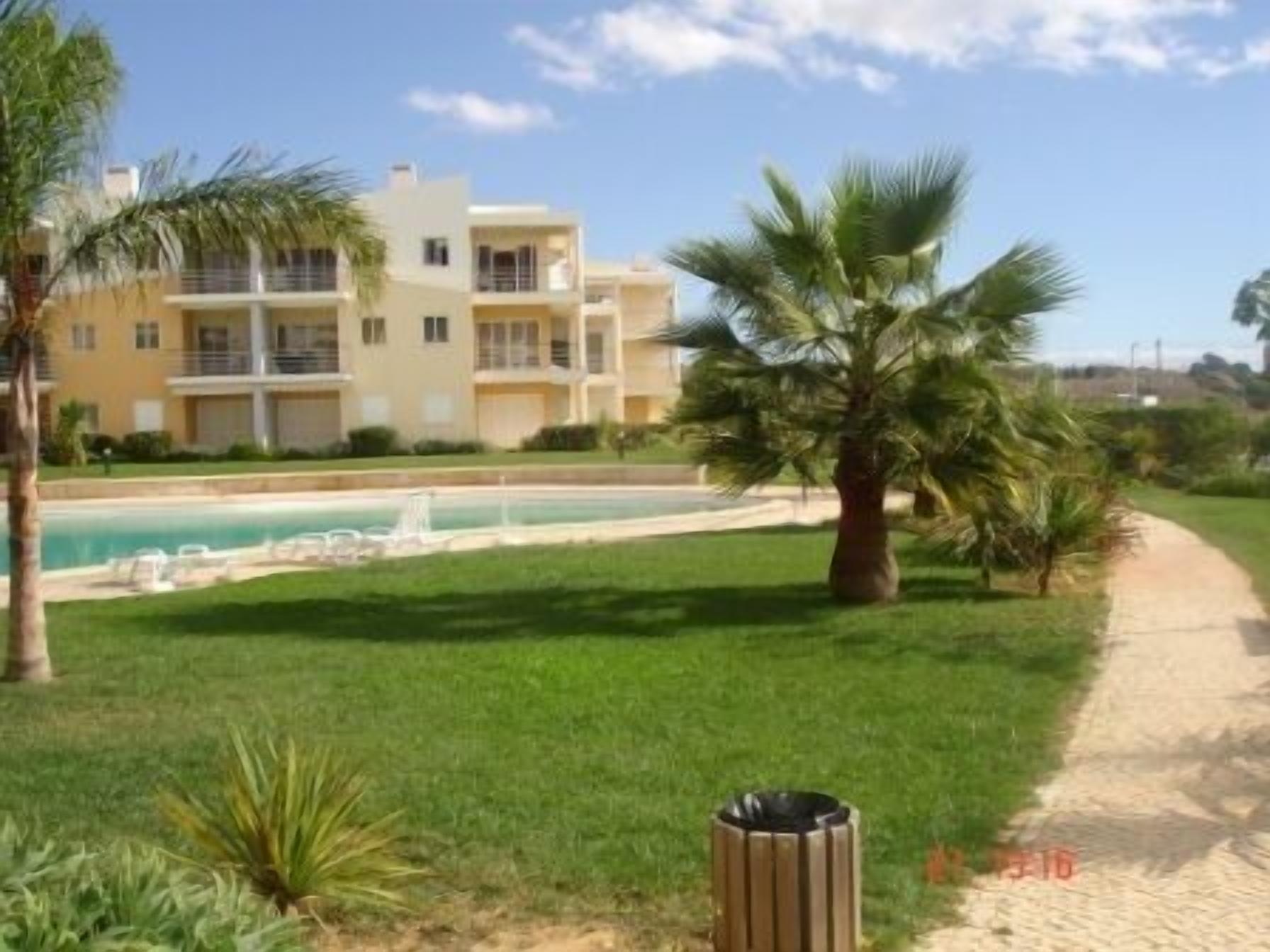 A residential building with a swimming pool, a pathway, and a palm tree.
