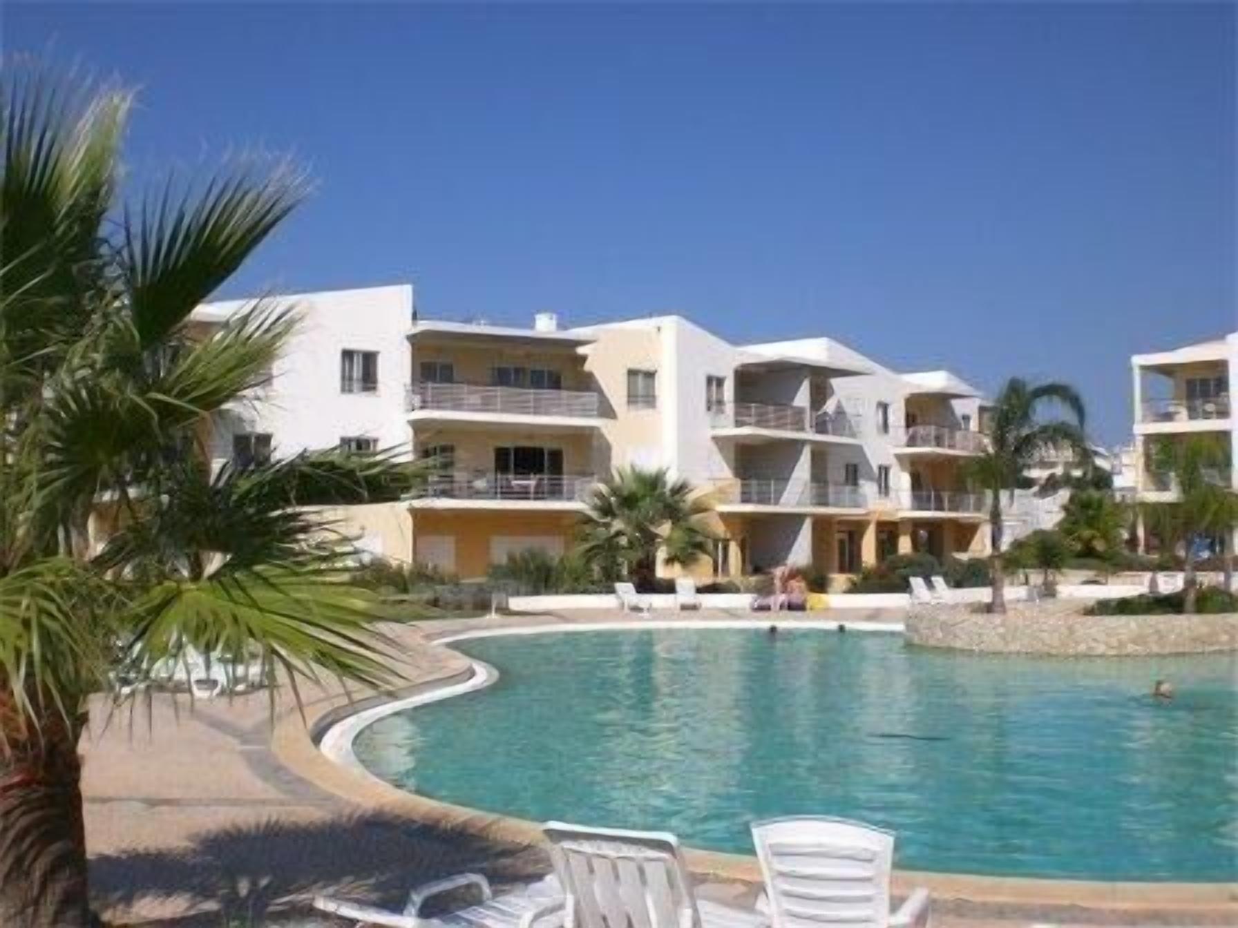 A resort with a swimming pool, multiple balconies, and palm trees.