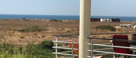 A balcony with a view of the sea, a red chair, and a table.