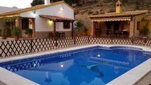 Une piscine entourée d’une clôture en bois, un espace patio et un bâtiment doté d’un toit en tuiles.