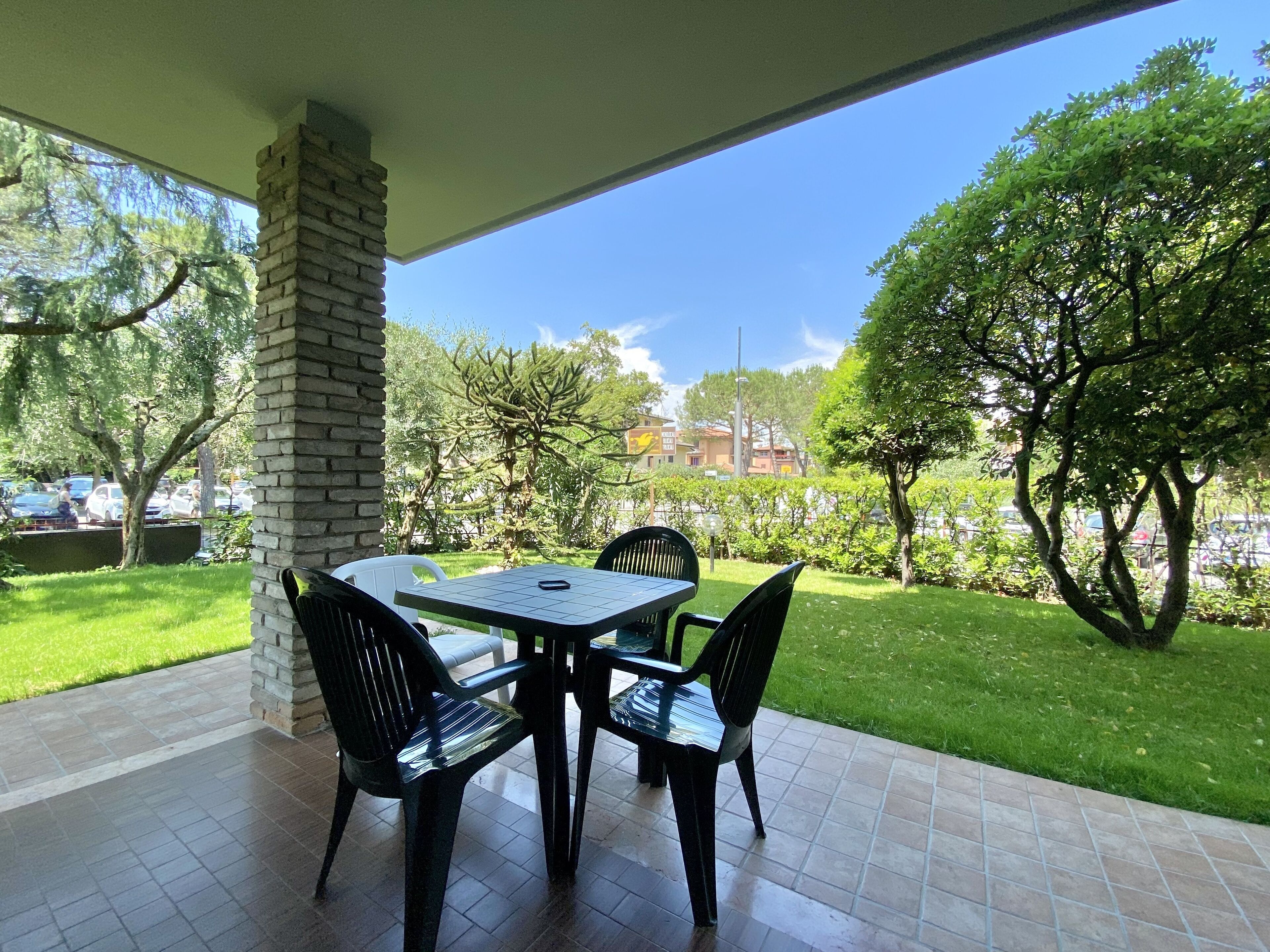 Une terrasse avec une table et des chaises, un pilier en pierre et une vue sur une pelouse verdoyante et des arbres.