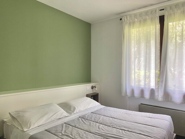A room with a bed, a nightstand, a window with curtains, and a radiator.