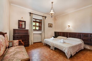 Une chambre à coucher avec un grand lit, une commode, une chaise, une fenêtre avec des rideaux, un radiateur et un lustre.