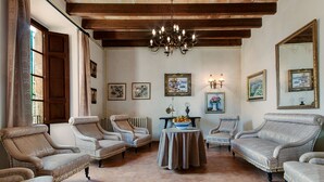Een ruime kamer met vier bekleden fauteuils, een ronde tafel met een schaal fruit, en een kroonluchter.
