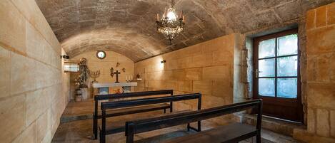 A church interior with stone walls, wooden pews, a chandelier, and a stained glass window.