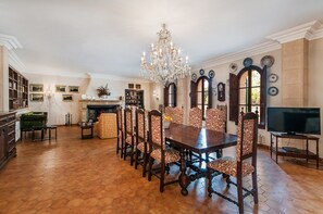 Une salle à manger avec une grande table en bois, des chaises à motifs, un lustre et une cheminée.