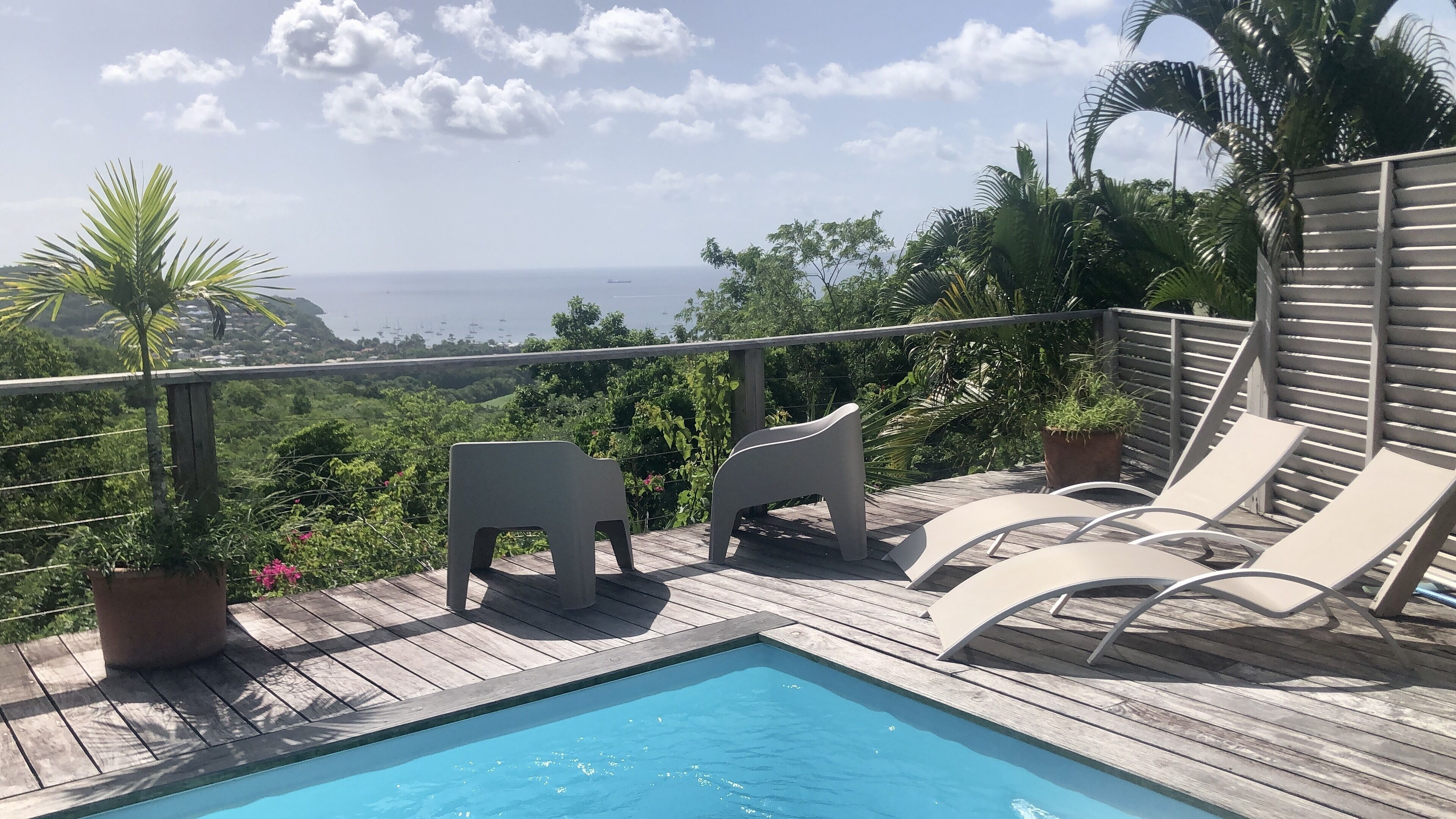 Una terraza de madera con piscina, sillas de descanso y vista al mar.