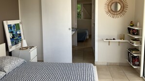 Un dormitorio con cama, mesita de noche, lámpara, unidad de aire acondicionado y un espejo en la pared.