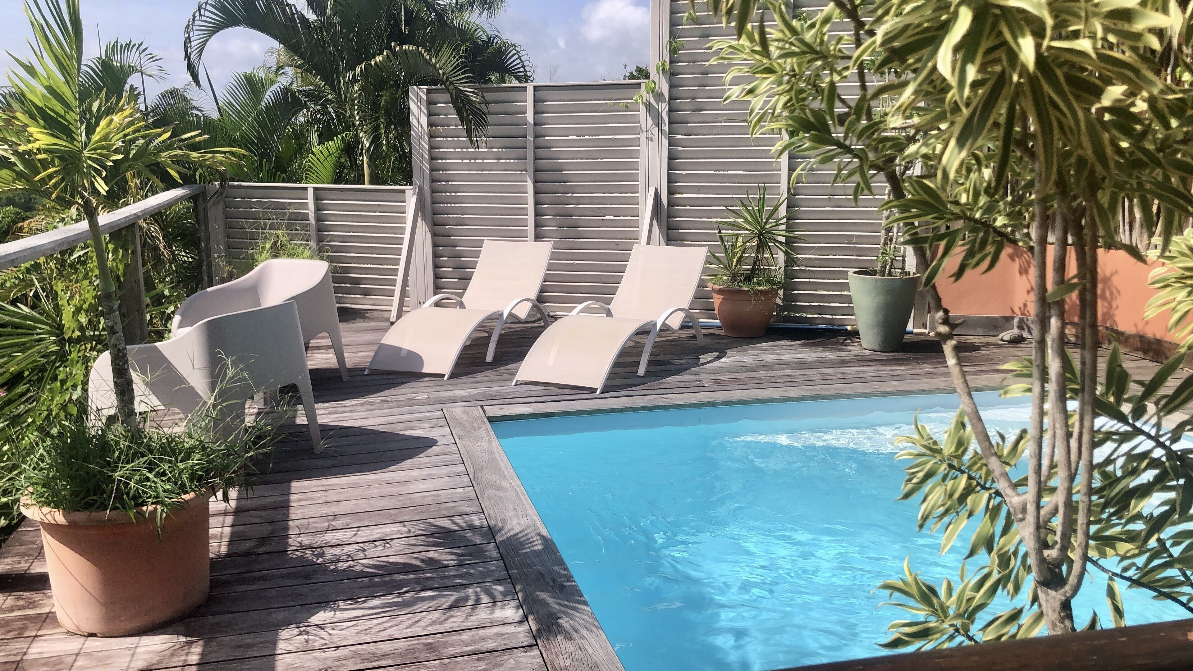 A wooden deck with a pool, lounge chairs, and potted plants.