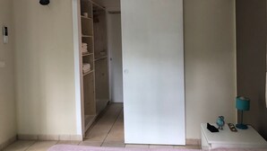 Una habitación con un armario de puerta corredera, una mesita con lámpara y un equipo de aire acondicionado en la pared.