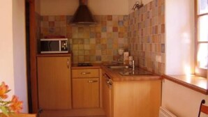 Eine kompakte Küche mit Holzausstattung, einer Mikrowelle und einer gefliesten Spritzschutzwand.