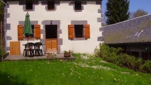 Ein zweistöckiges Haus mit Steinaußenwand, Holzhörnern und einer kleinen Veranda mit Gartenmöbeln.