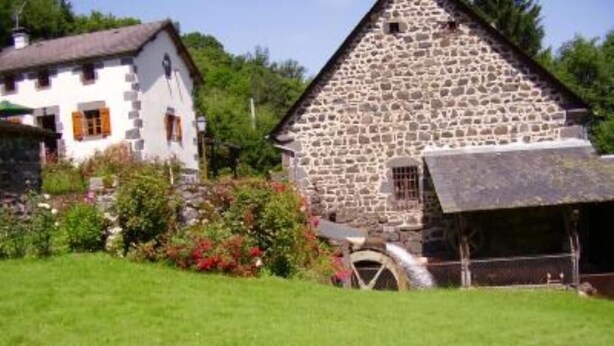 Ein Steinhaus mit einem Strohdach, umgeben von einem gepflegten Garten und einer Wiese.