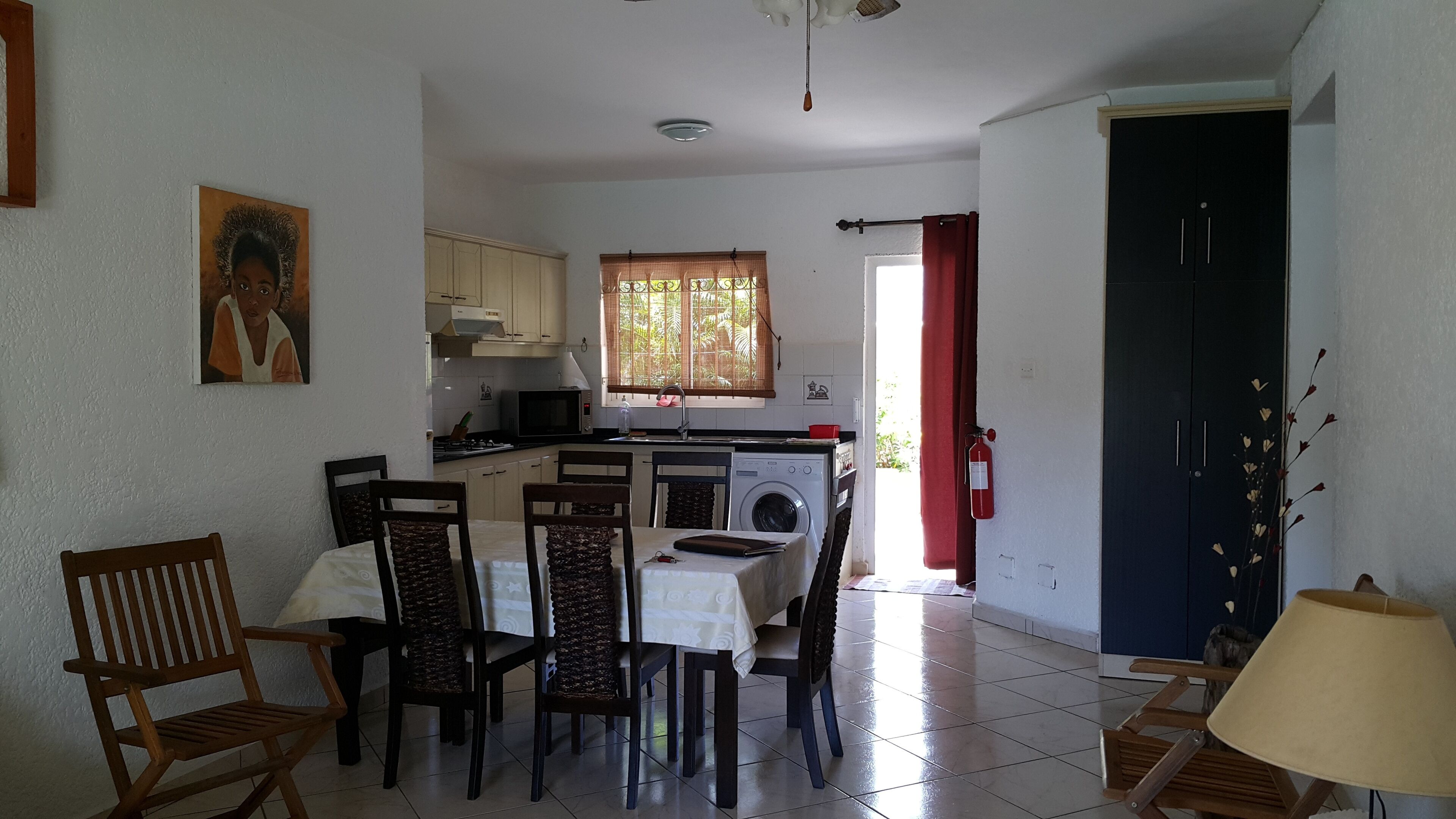 Una cocina compacta con lavadora, una mesa de comedor con sillas y una puerta roja.