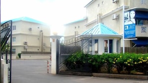 Une entrée fermée par un portail, donnant sur un bâtiment doté d’un toit bleu, d’une enseigne et d’une banderole.