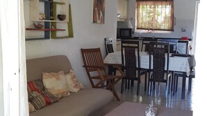 Un salon avec un canapé, une table à manger avec des chaises, un coin cuisine et une petite table à manger recouverte d’une nappe.