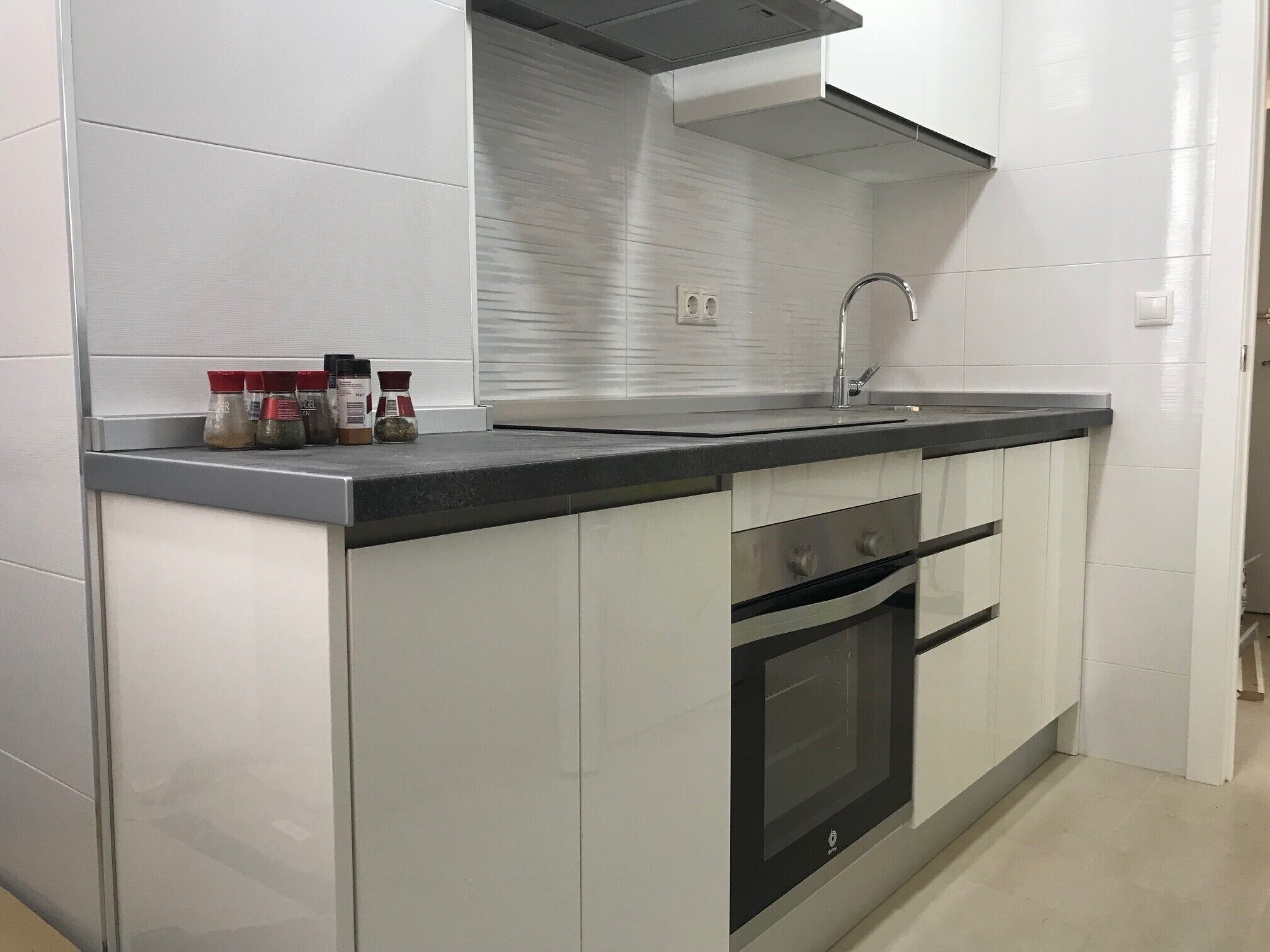 A kitchen with white cabinets, a stainless steel countertop, a built-in oven, and a stainless steel sink.