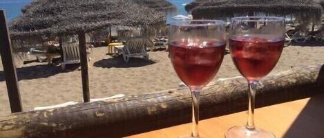 Two wine glasses on a wooden table with a beach view.