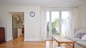 A spacious living area with a wooden floor, a sofa, a coffee table, and a sliding glass door leading to a balcony.
