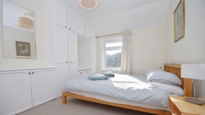 A bedroom with a bed, a bedside table, a nightstand, a window with curtains, and a wardrobe.