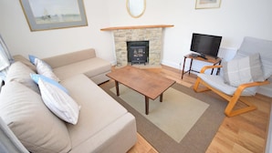 A living room with a stone fireplace, a television on a wooden table, a sofa, and a chair.