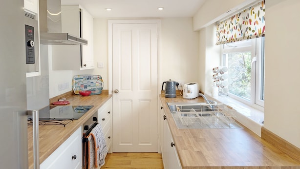 A modern kitchen with white cabinets, a wooden countertop, a kettle, a toaster, and a window with a colorful curtain.