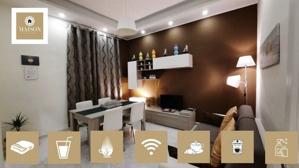 A modern living room with a dining area, a sofa, a TV, and a lamp. There are decorative items on a shelf and a plant on the floor. - LA MAISON SR Cozy apartment in the center of town (Campobasso)