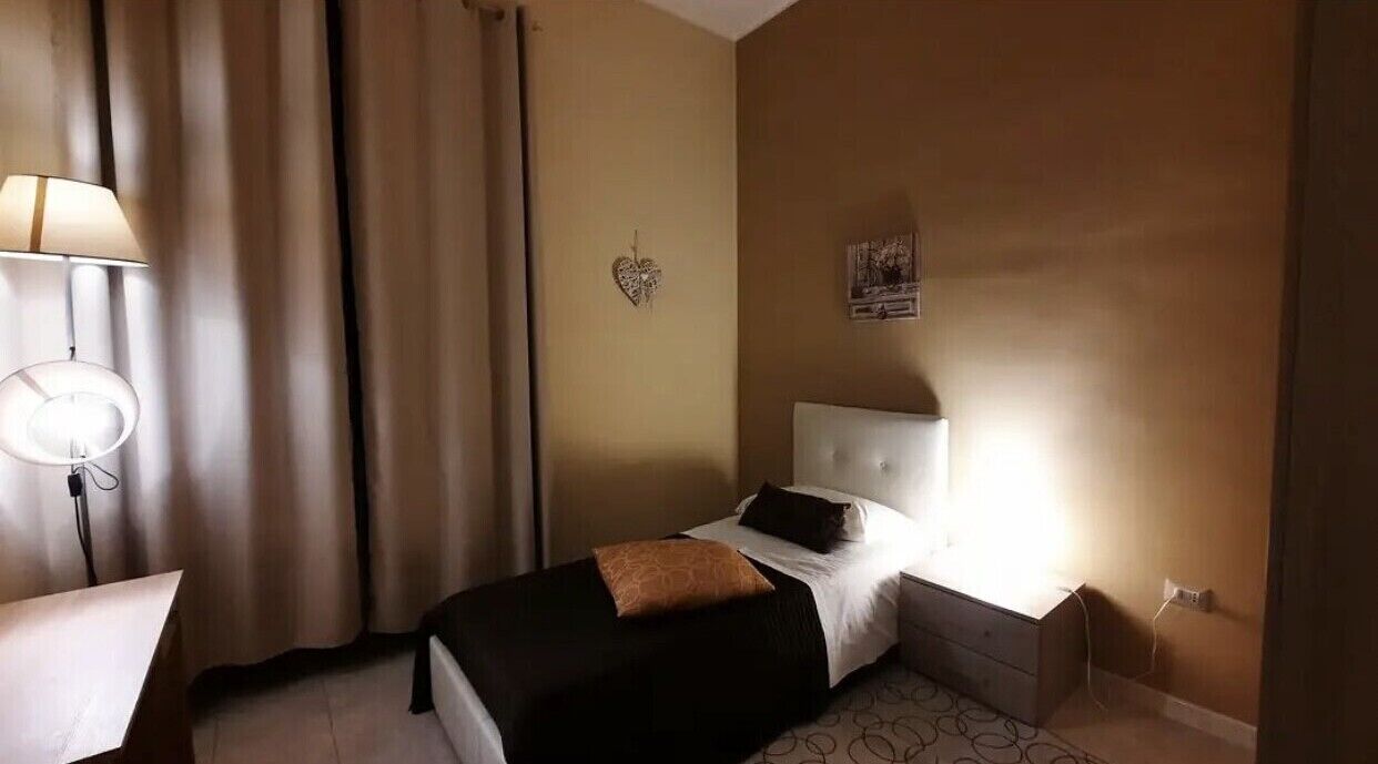 A hotel room with a bed, a desk, a lamp, and a wall-mounted heart-shaped decoration.