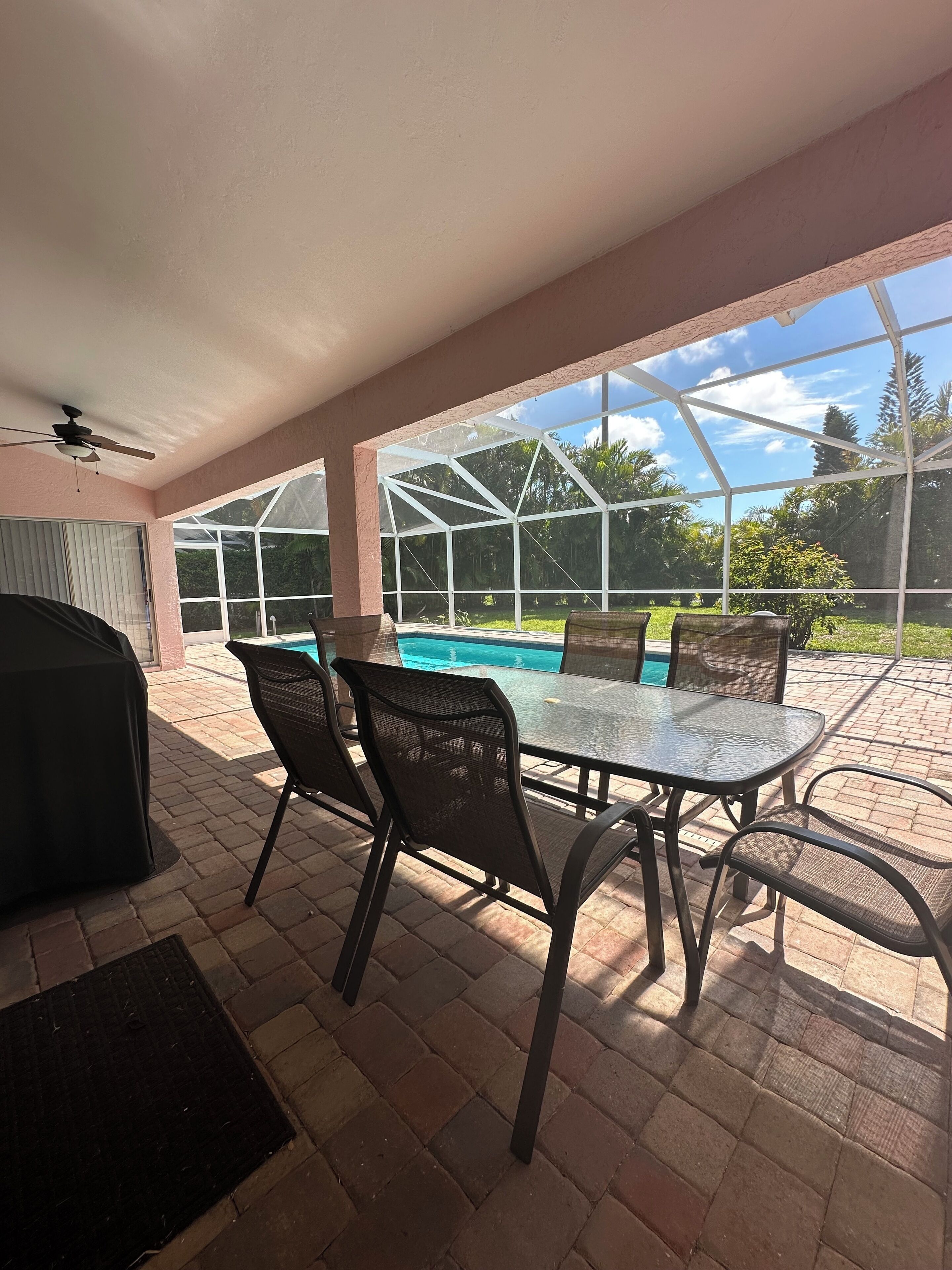 Une terrasse extérieure dotée d’une piscine protégée par des parois en verre, d’un espace barbecue couvert et d’une table avec des chaises.