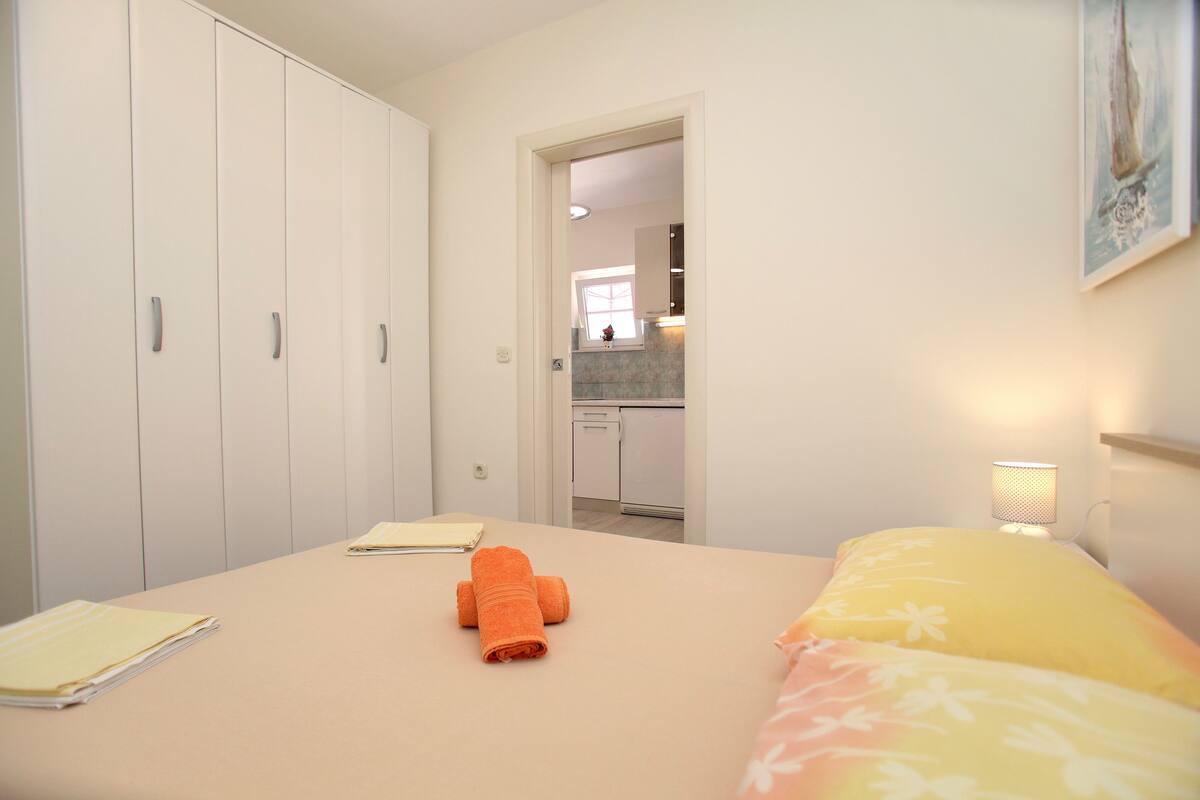 A bedroom with a bed, a nightstand, a desk with a chair, and a wardrobe.