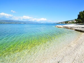 A clear coastal beach with a pebble shore and a distant shoreline. - Apartments Viki (Trogir)